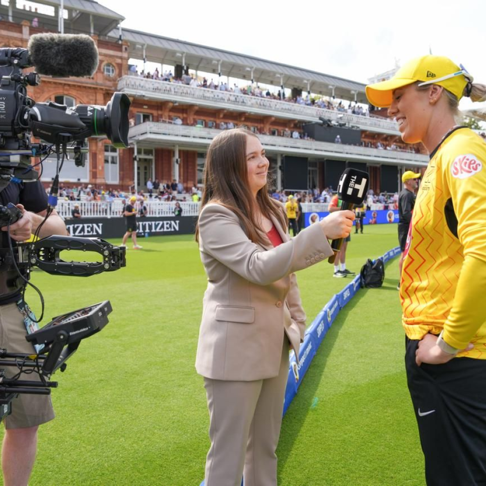 camera in left corner, with the young female broadcaster winner and a cricketeer doing an interview
